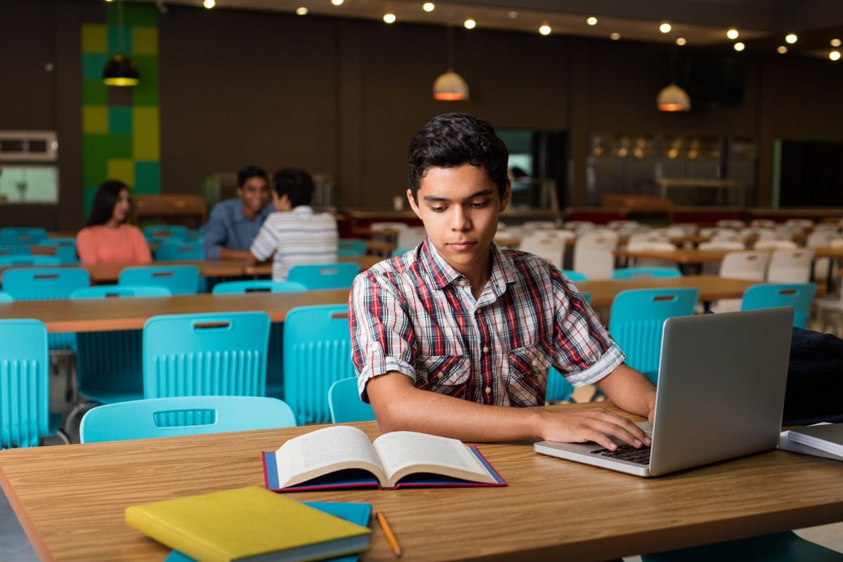 Estudiante con laptop y libros en una biblioteca